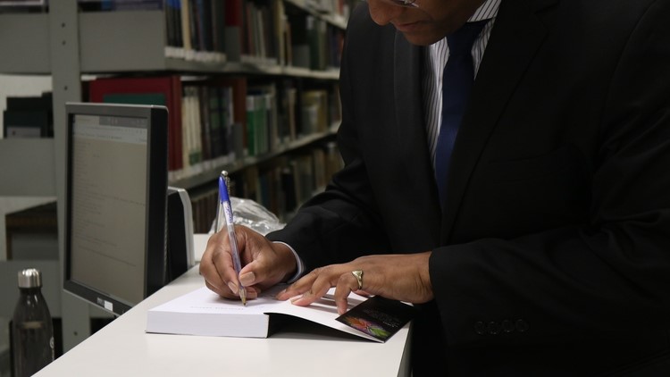 Autor escrevendo dedicatória no livro doado à Biblioteca.