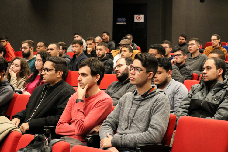 Plateia de alunos, sentados em cadeiras vermelhas, acompanhando atentamente a palestra no auditório do Centro Universitário Assunção.