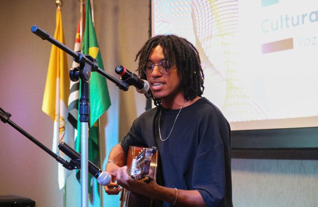 Aluno se apresenta musicalmente com voz e violão, encantando o público presente.