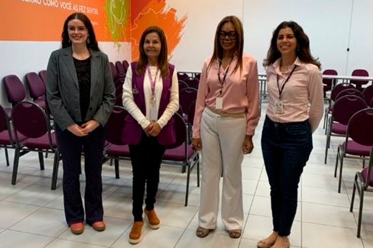 Prof.ª Dr.ª Karen Ambra, Reitora do Centro Universitário Assunção; Lucia Brugnera, gestora da Casa da Mulher Brasileira; Dr.ª Regina Célia da Silveira Santana, Secretária Municipal de Direitos Humanos e Cidadania de São Paulo; e Dr.ª Stella Verzolla, Secretária Adjunta. As quatro posam para foto em uma sala com cadeiras dispostas ao fundo e um painel com mapa e texto institucional na parede.