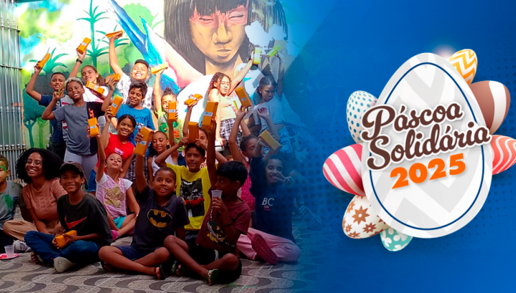 Crianças sorridentes posam segurando chocolates arrecadados pela campanha Páscoa Solidária 2025, sentadas em frente a um mural colorido com arte urbana. Ao lado direito da imagem, sobre um fundo azul, aparece o logo da campanha com ovos decorados e o texto “Páscoa Solidária 2025”.