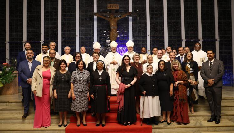 Grupo de pessoas reunidas na escadaria de uma igreja, com padres, bispos e religiosos ao centro, diante de um crucifixo, todos posando para foto após uma cerimônia.